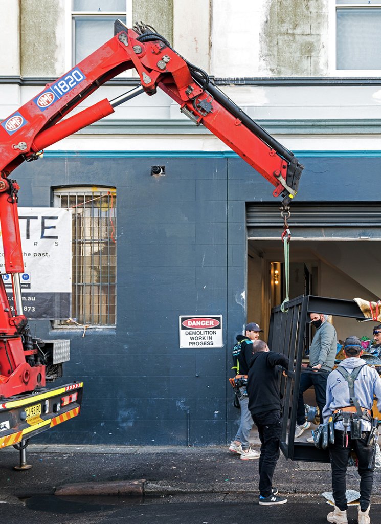 A red crane is pushing a black frame while several tradies are gathered around it.