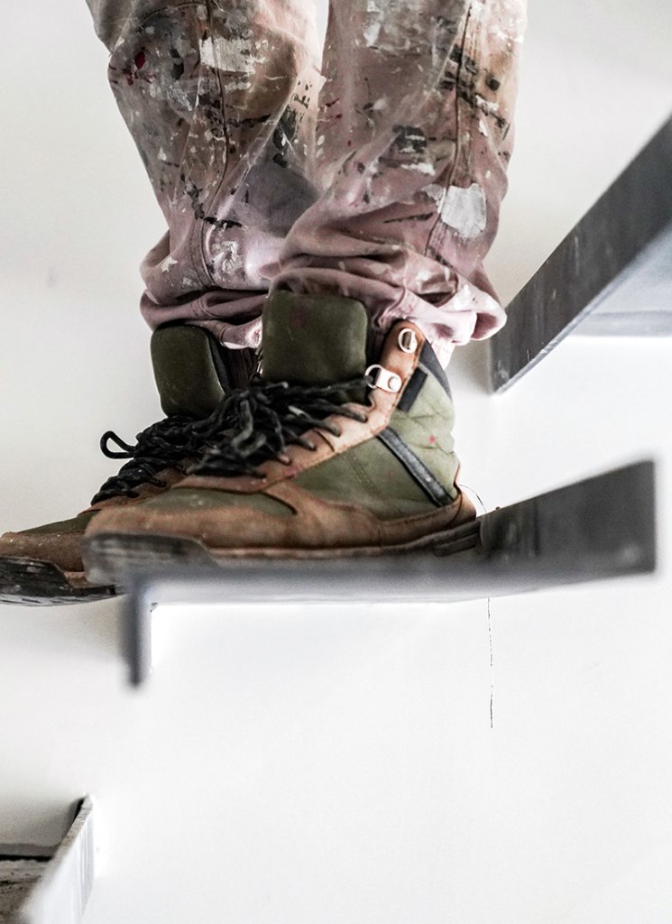 A painter is on the stairs wearing green shoes and a tan outfit with paint stains on their pants.