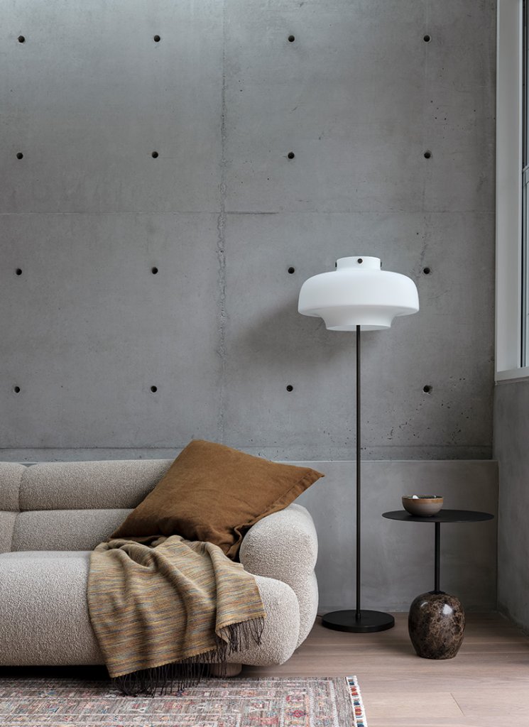 In this room, a concrete wall catches the light. A cream sofa with boucle fabric from Jardan Furniture sits on a timber floor by Tongue n Groove Australia. A rug from Hali Rugs completes the space.