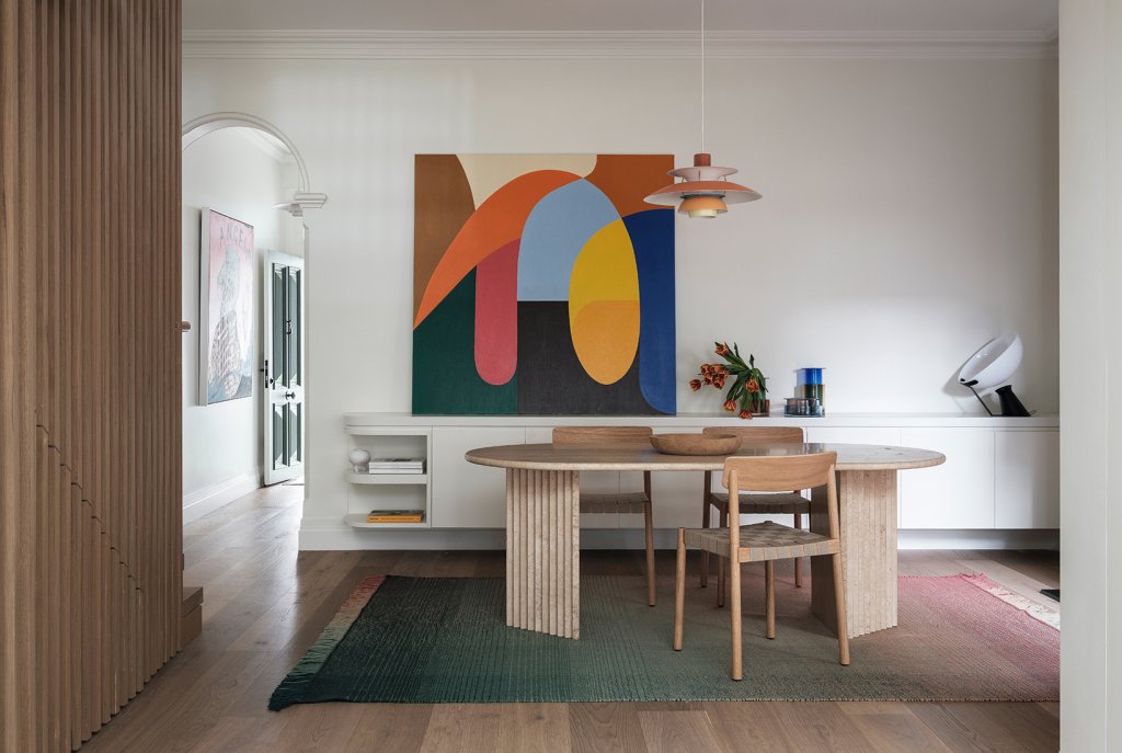 Dining area in the Leichhardt House,The walls are adorned with vibrant art pieces by Stephen Ormandy, in built buffet in White, slatted panel in timber, light Louis Poulsen by Cult design, and Timber Floor by Tongue n Groove Australia.