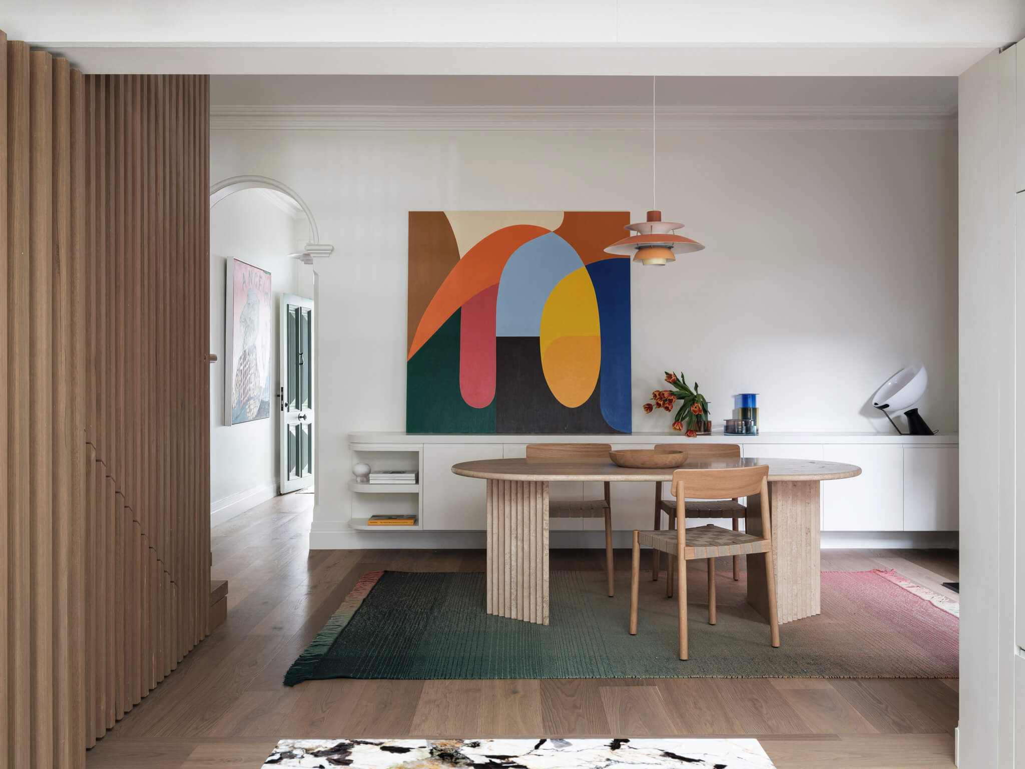 Dining area in the Leichhardt House,The walls are adorned with vibrant art pieces by Stephen Ormandy, in built buffet in White, slatted panel in timber, light Louis Poulsen by Cult design, and Timber Floor by Tongue n Groove Australia.